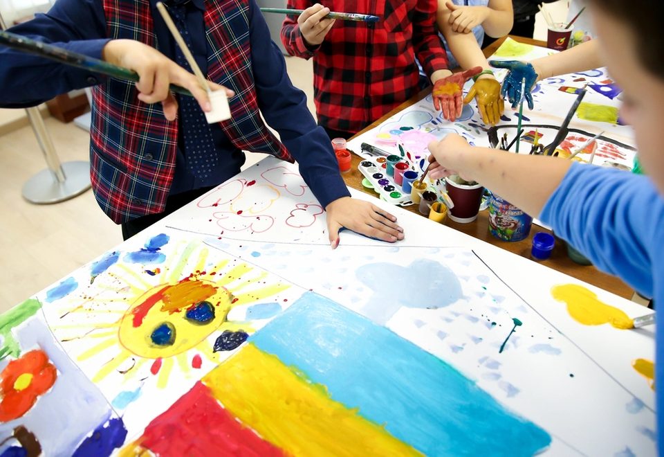 Children's paint-covered hands reaching across bright finger paintings.
